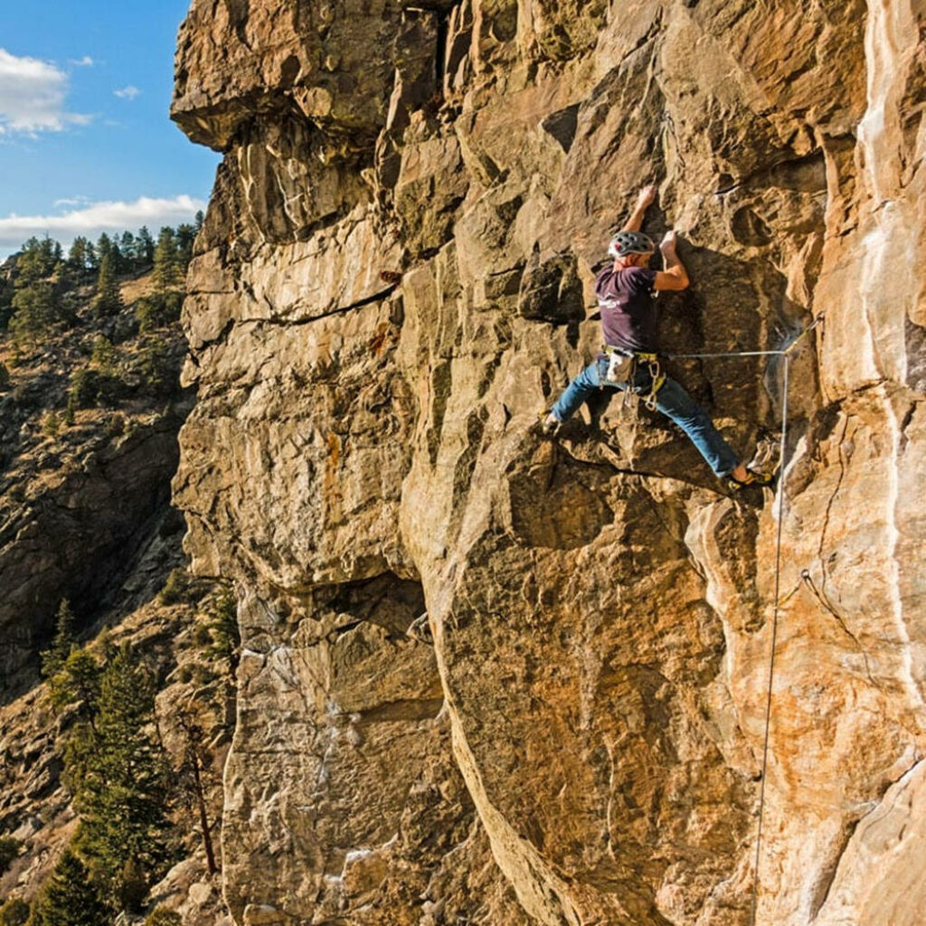 Sport climber ascending rugged rocky cliff with scenic nature and clear blue sky background Wallpaper