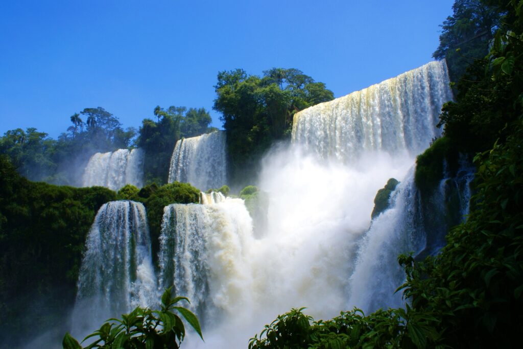 Thundering waterfalls cascading down lush green cliffs under vibrant blue sky natural landscape Wallpaper