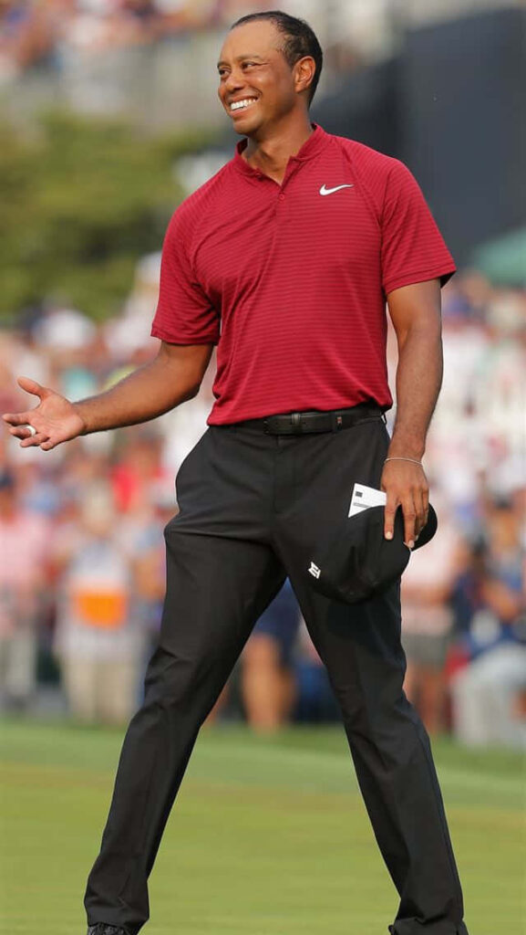 Tiger Woods smiling confidently in red polo and black pants on golf course wallpaper background
