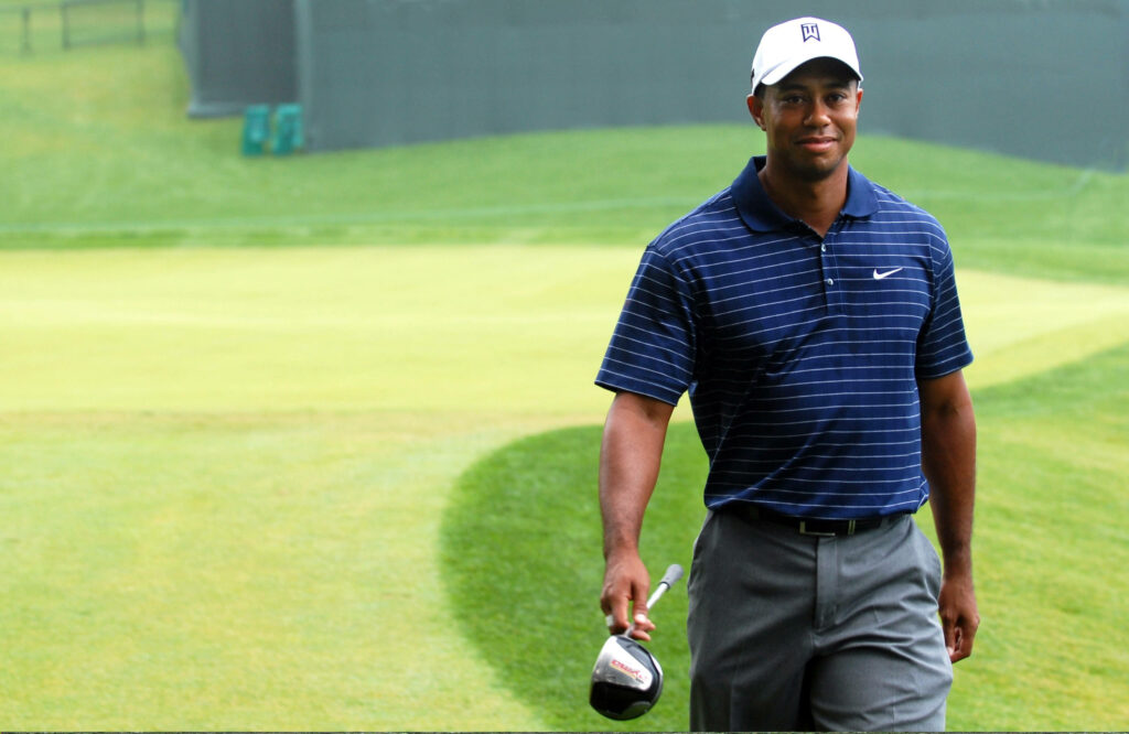 Tiger Woods confidently walking on golf course in signature attire holding golf club wallpaper