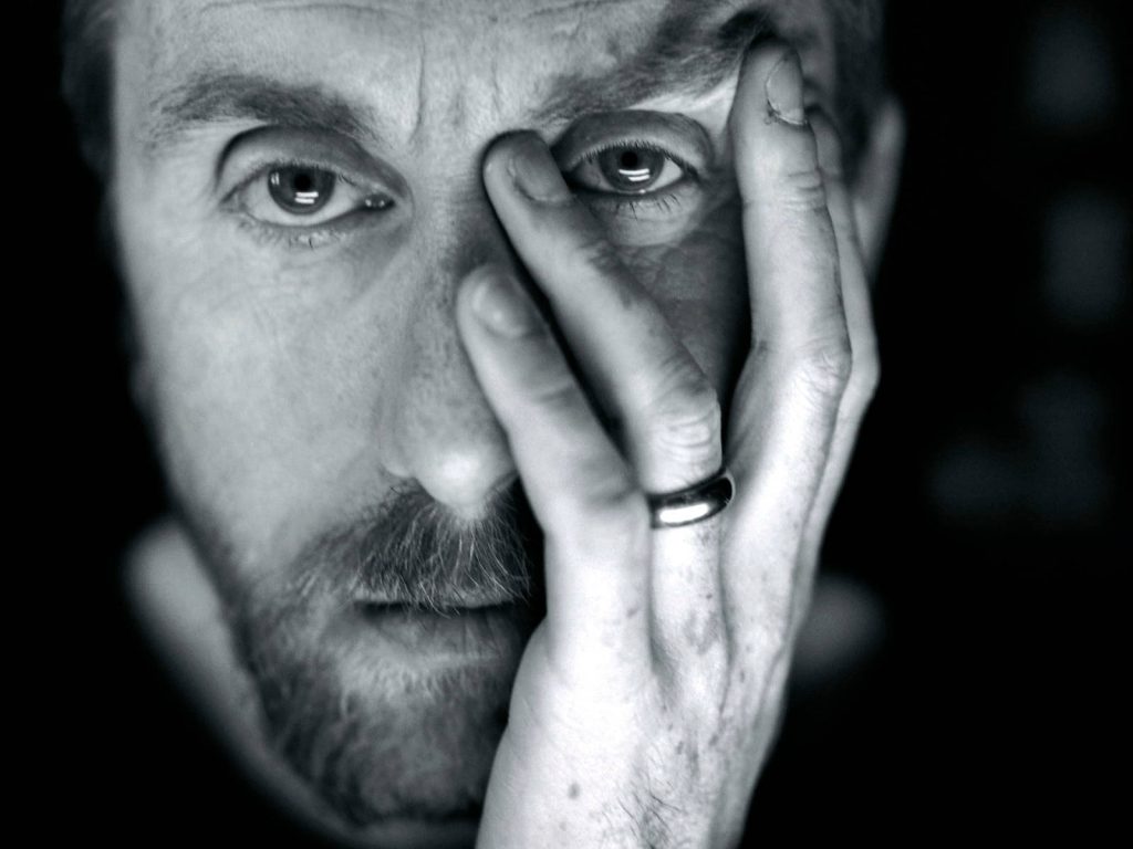 Close-up black and white portrait of actor Tim Roth with hand on face in moody lighting wallpaper