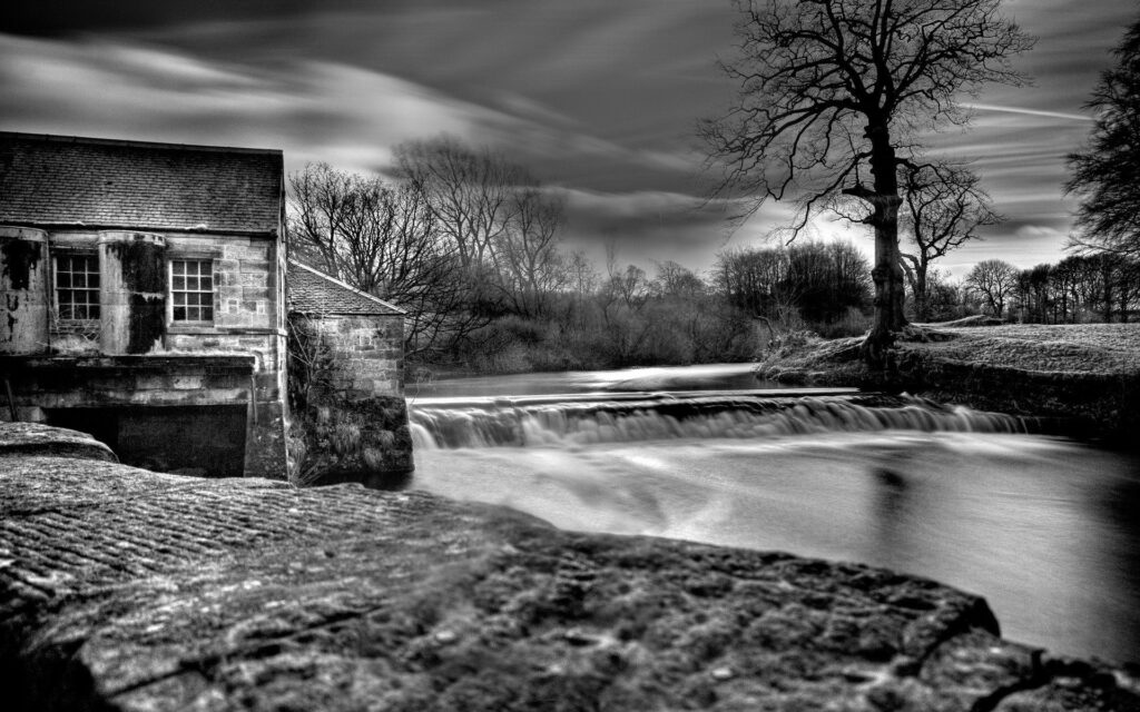 Black and white riverside wallpaper with historic house dam flowing water bare trees classic charm