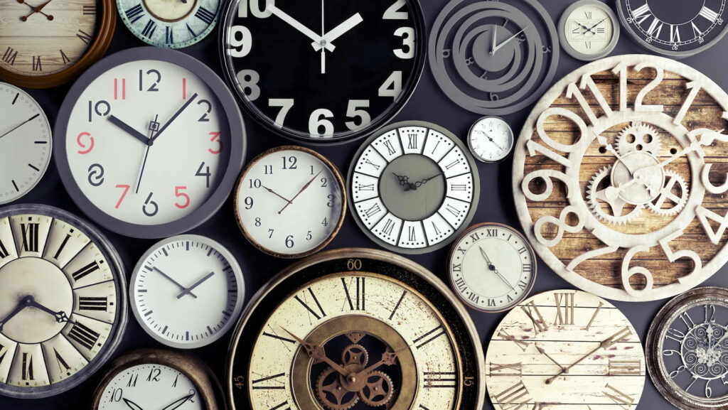 Flat lay of diverse vintage and modern circular analog clocks in neutral and metallic tones wallpaper
