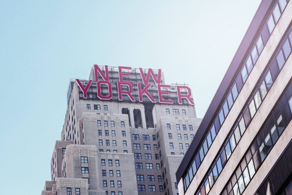 New Yorker Hotel red sign on historic Art Deco building with hazy blue sky wallpaper background