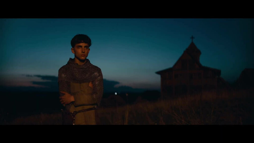 Timothée Chalamet in chainmail armor gazing at dusk near rustic wooden building wallpaper background