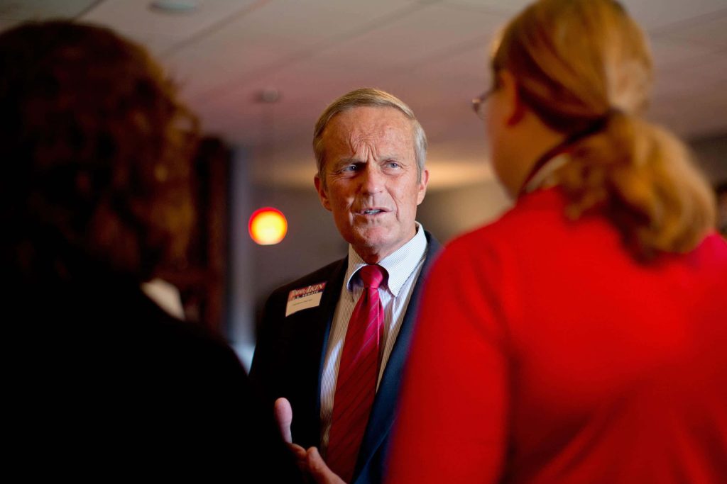 Todd Akin speaking at campaign event in dark suit red tie news style wallpaper background