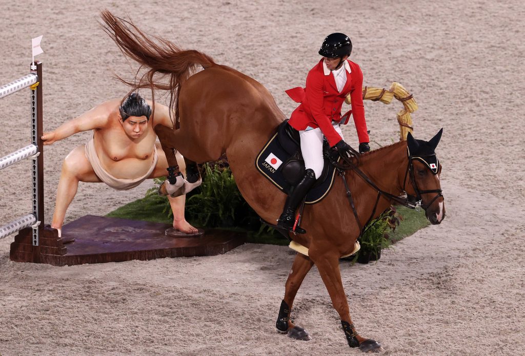 Japanese equestrian athlete in red jacket jumps chestnut horse over Sumo wrestler obstacle Tokyo 2020 Wallpaper
