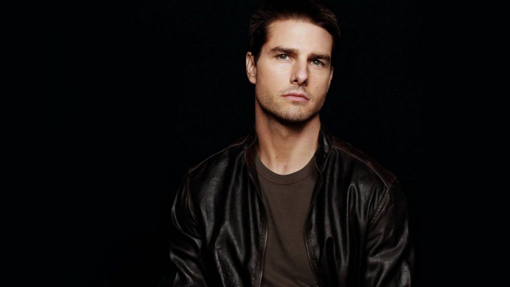 Tom Cruise portrait wallpaper in leather jacket with intense gaze on black background HD image
