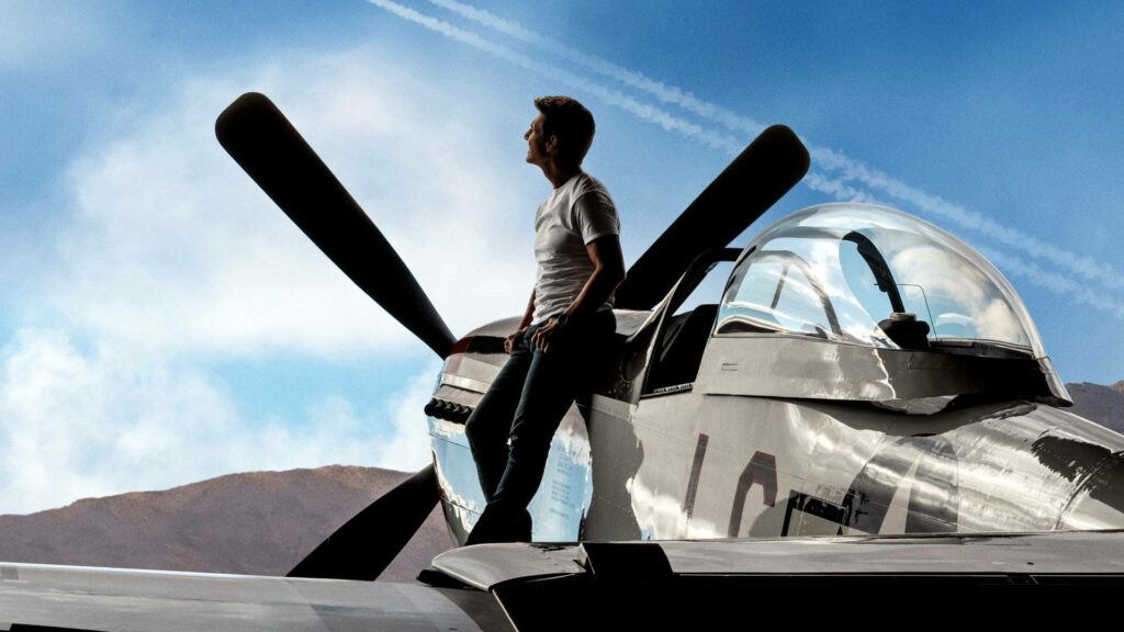 Tom Cruise as Pete Mitchell stands confidently by jet plane Top Gun Maverick wallpaper background