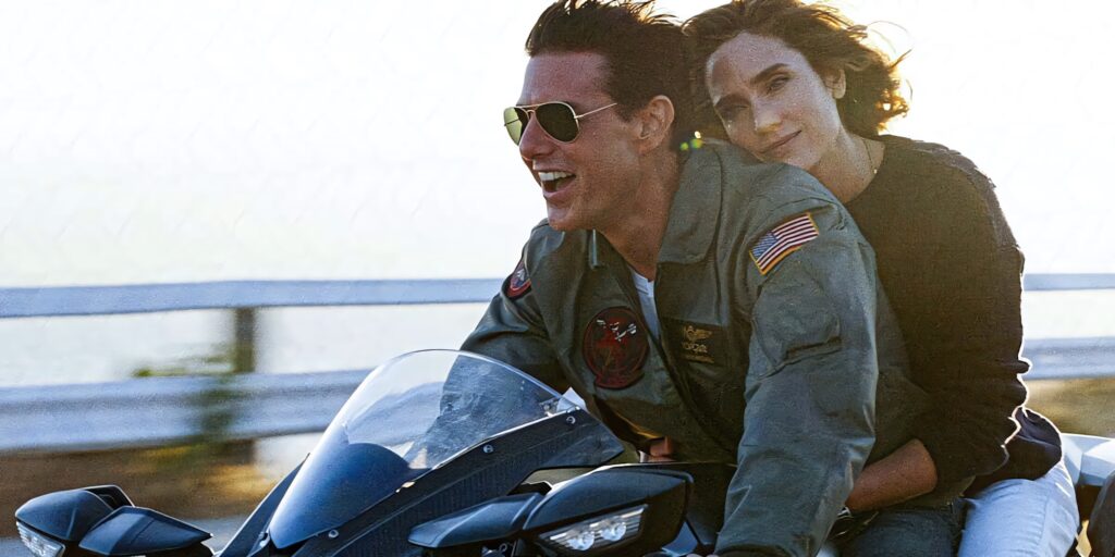 Tom Cruise as Pete Mitchell rides motorcycle with passenger along coastal road Top Gun Maverick Wallpaper