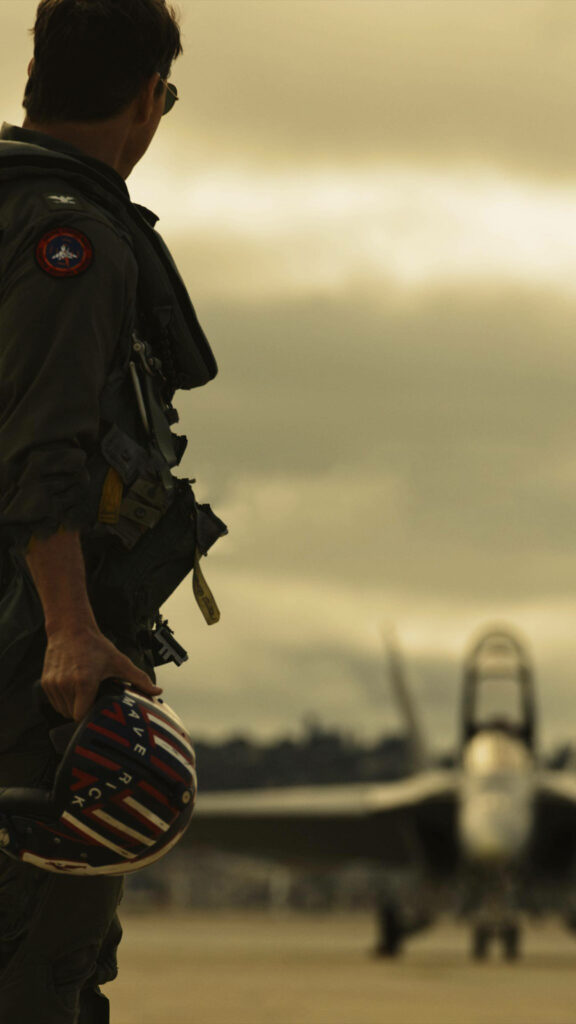 Tom Cruise as Pete Mitchell in flight suit holding helmet on runway near fighter jet Top Gun Maverick Wallpaper