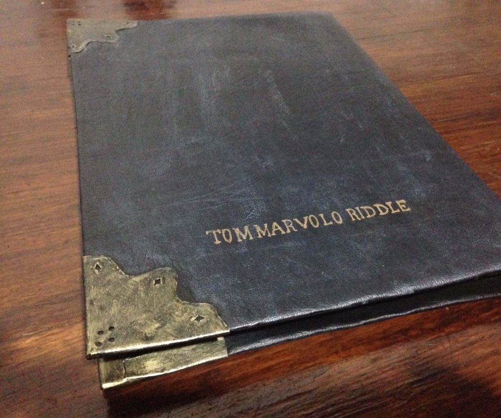 Tom Marvolo Riddle diary Horcrux Harry Potter black leather book with gold text on wood Wallpaper