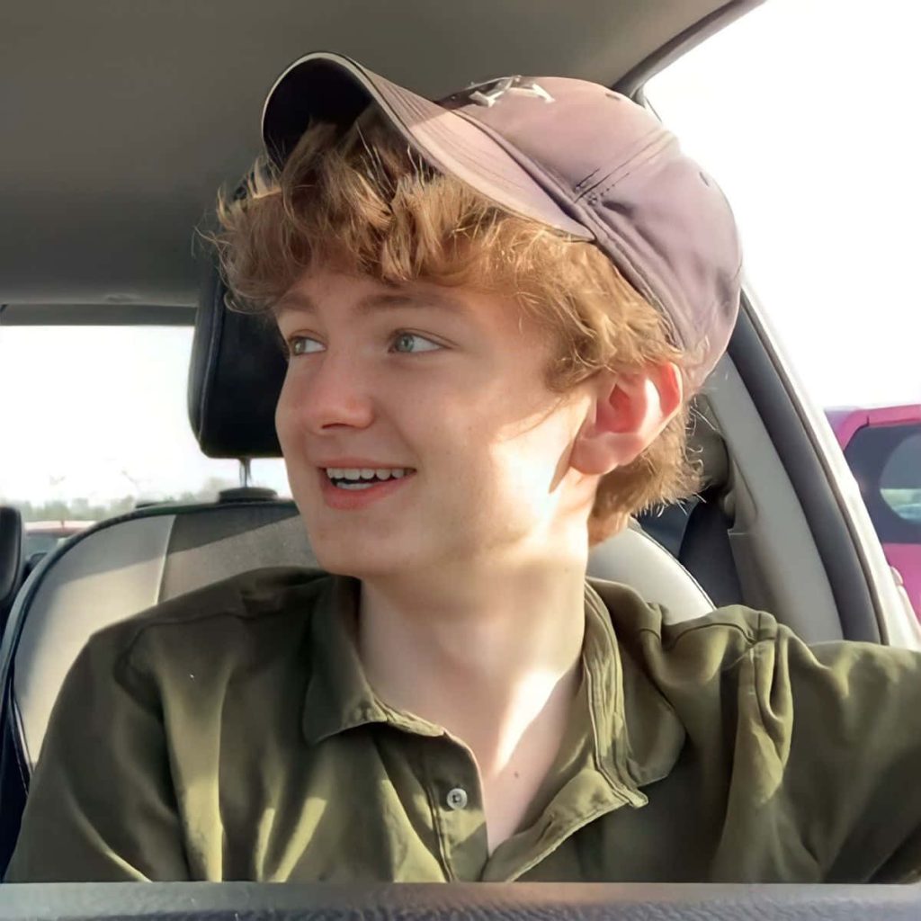 TommyInnit relaxed in car wearing olive shirt grey cap warm natural light blonde hair wallpaper
