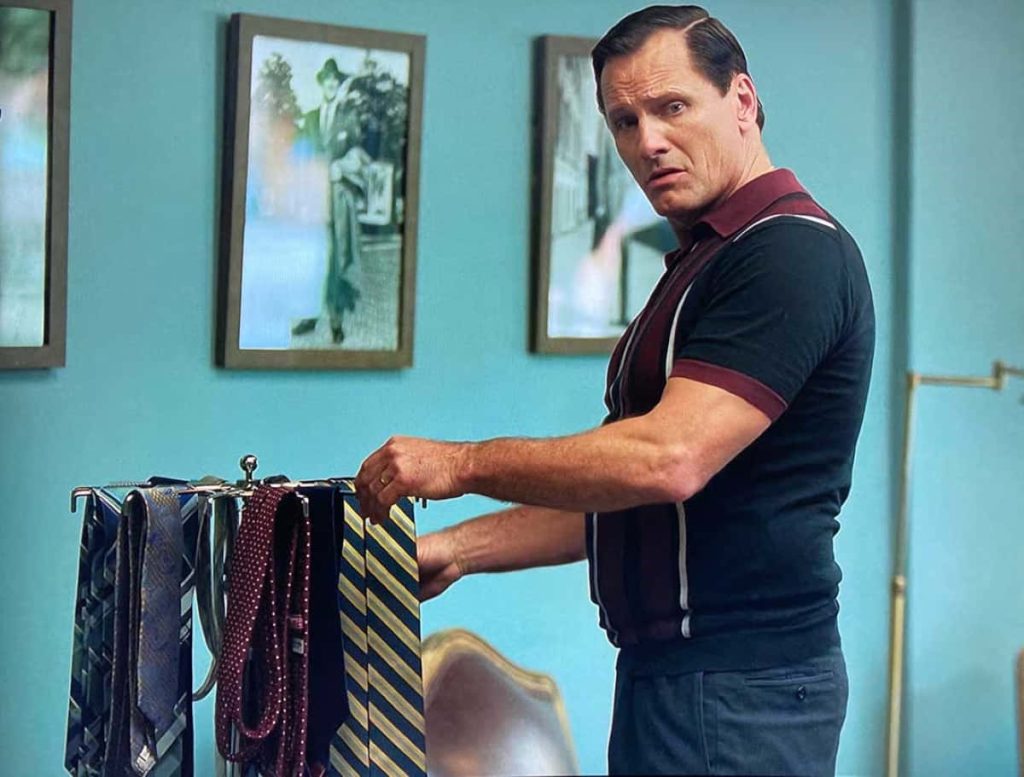Viggo Mortensen as Tony Lip choosing necktie in retro 1960s room with vibrant blue wall wallpaper