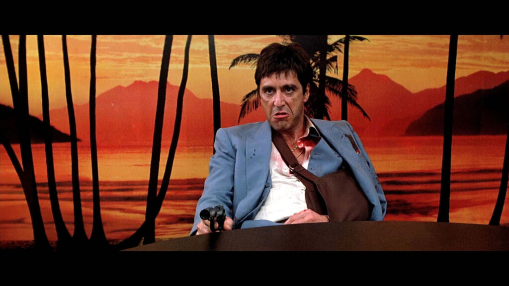 Tony Montana holding gun at desk during dramatic sunset Scarface iconic movie wallpaper background