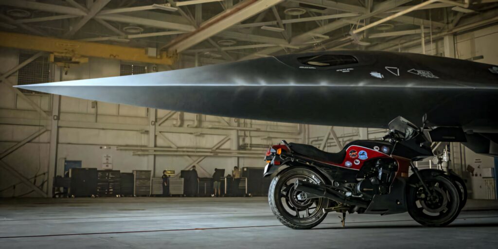 Top Gun Maverick wallpaper Pete Mitchell motorcycle under futuristic Darkstar jet in hangar background