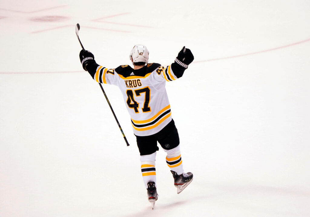 Torey Krug Boston Bruins celebrates game winning goal with arms raised on white ice background Wallpaper