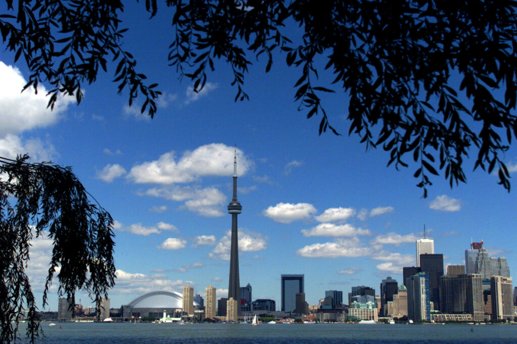 Panoramic view of CN Tower and Toronto skyline framed by trees under bright blue sky clouds Wallpaper