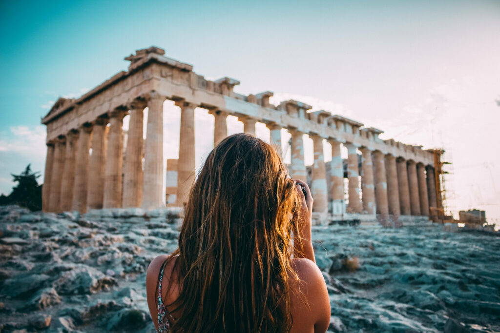 Tourist girl photographing Parthenon at Athens ancient stone ruins during sunset soft light Wallpaper