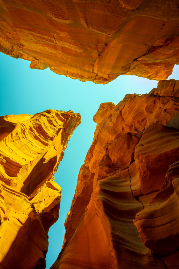 Bottom view of towering canyon rocks with warm orange hues and vibrant blue sky background Wallpaper
