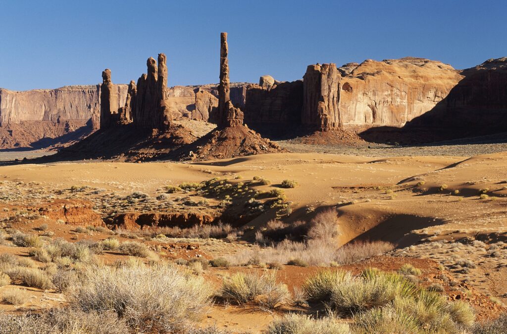 Towering canyon walls rugged rocks desert vegetation soft sand clear blue sky wallpaper