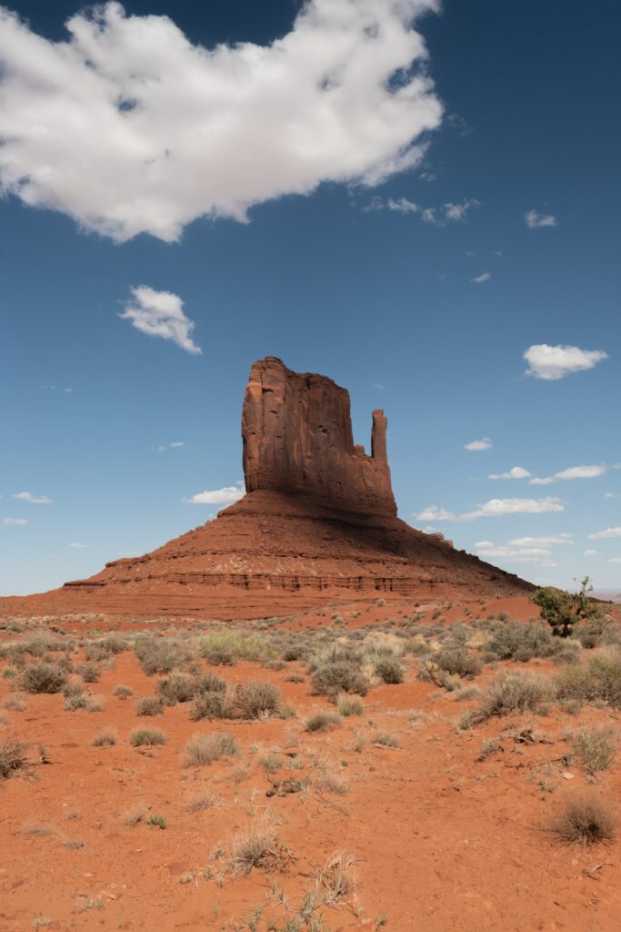Towering rock formation in desert canyon under blue sky with clouds dramatic natural landscape Wallpaper