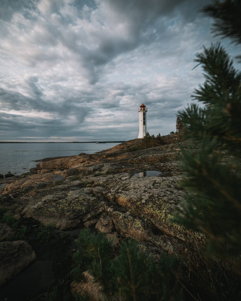 White lighthouse on rocky coast under dramatic sky with turbulent blue ocean wallpaper background