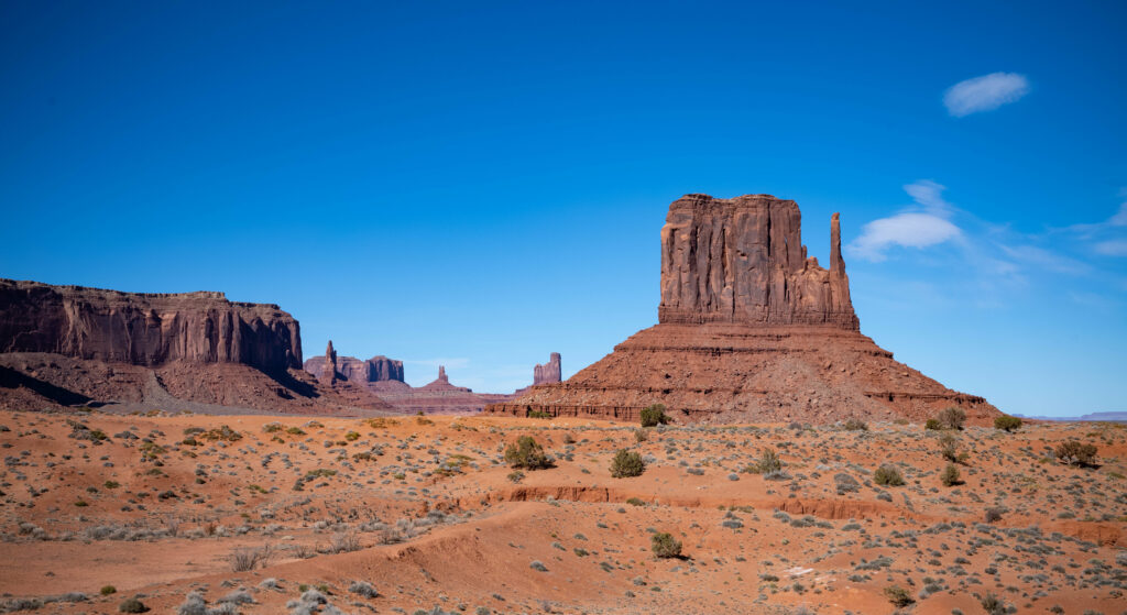 Towering red rock formations in desert with green bushes under bright blue sky wallpaper background