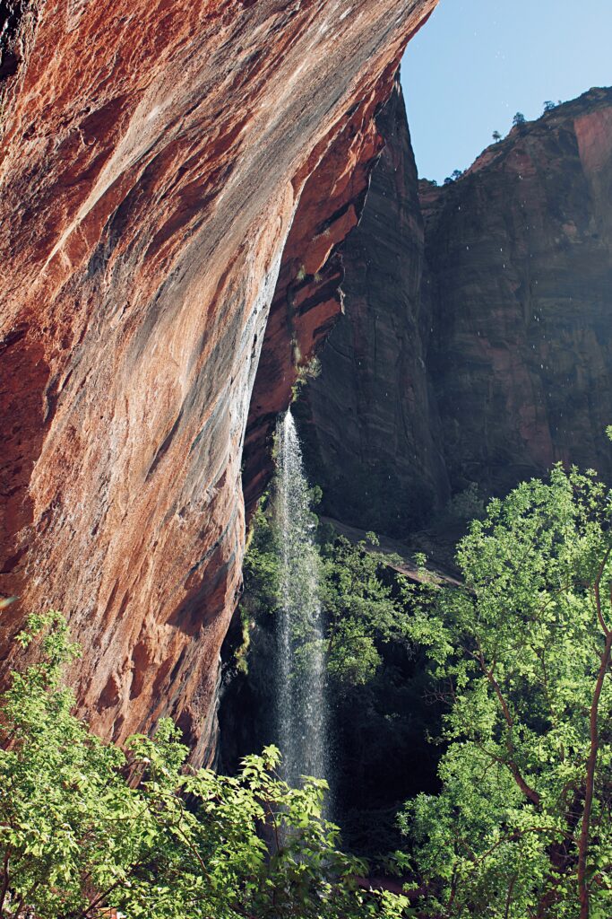 Towering red rocks and slender waterfall beside lush greenery in a dramatic natural landscape wallpaper