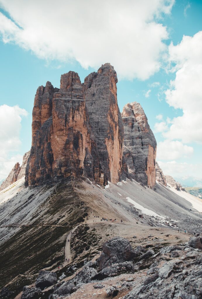 Towering rock formations and rugged mountain peaks under bright blue sky with scattered clouds Wallpaper
