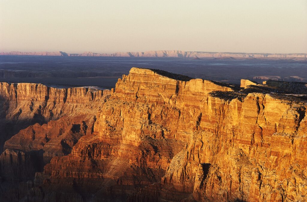 Towering rocky cliffs in warm evening light with dramatic shadows over a hazy landscape wallpaper