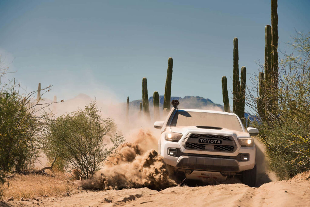 Toyota TRD driving through sandy desert dunes with cacti and clear blue sky background Wallpaper