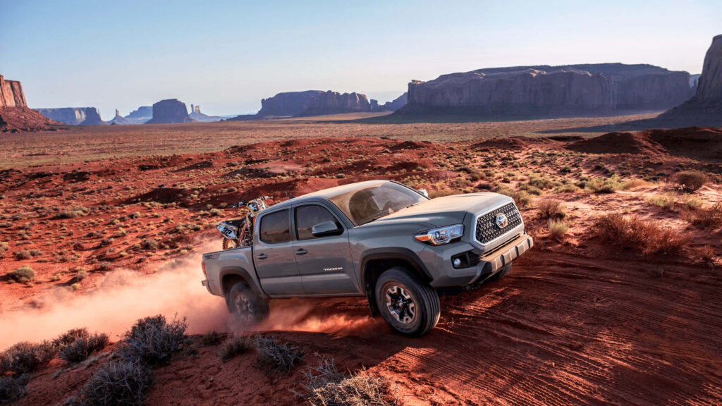 Toyota TRD pickup truck speeding through rugged desert terrain kicking up red dust under blue sky Wallpaper