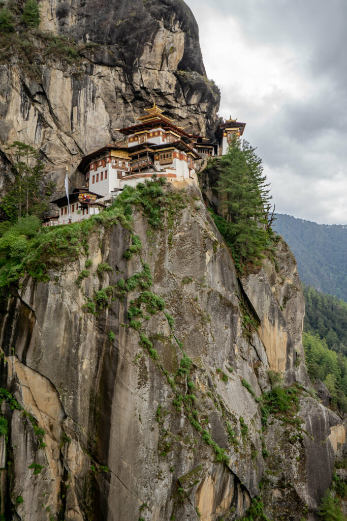 Traditional building on rocky cliffs with lush greenery and misty mountains wallpaper background