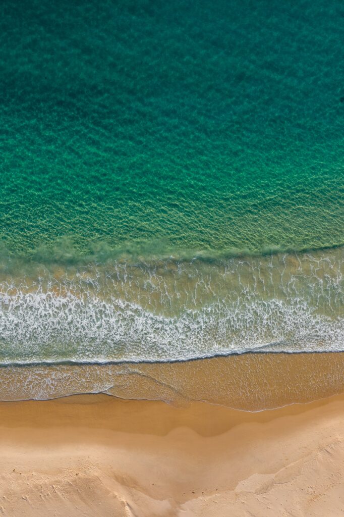 Aerial view of turquoise waves gently meeting golden sand on a tranquil beach wallpaper background