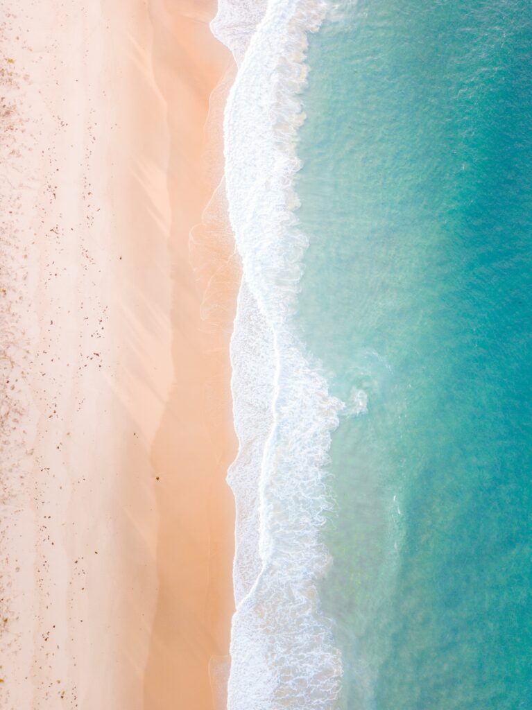 Aerial view of tranquil beach with turquoise waves and soft sandy shores pastel coastal wallpaper