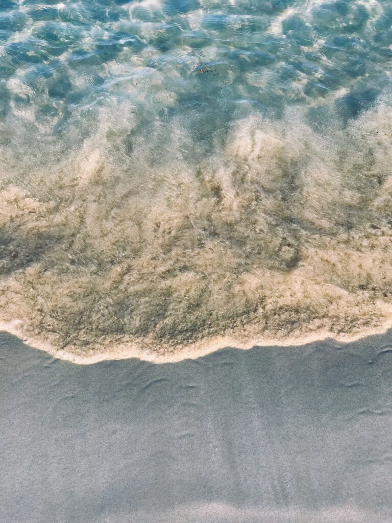 Aerial view of clear ocean waves gently meeting soft sandy beach with natural color gradient Wallpaper
