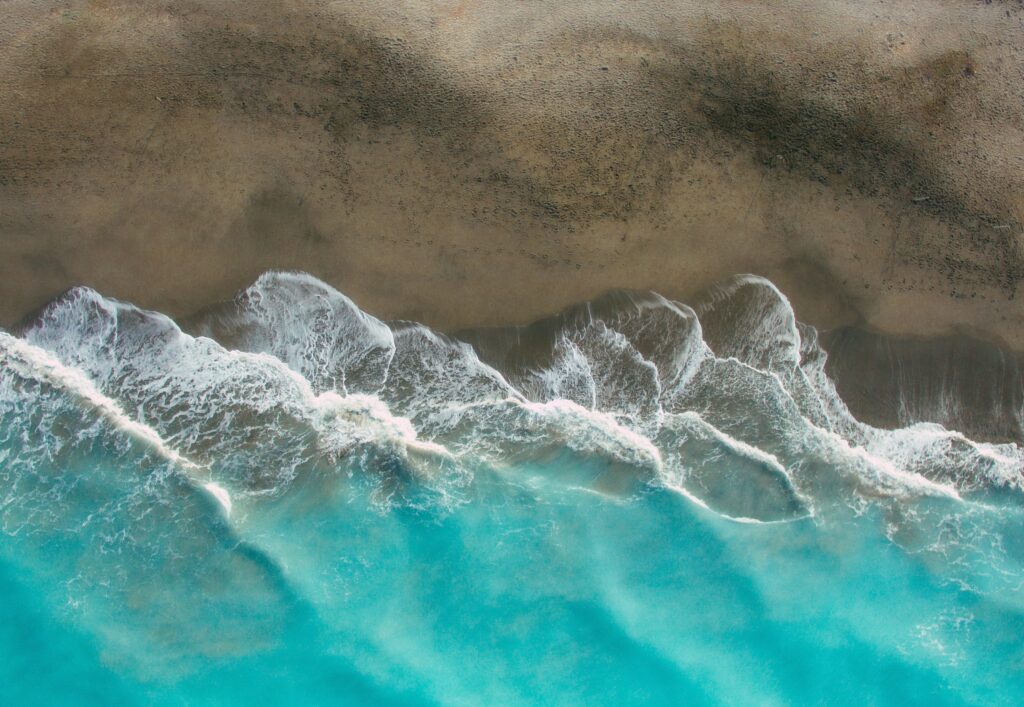Aerial view of serene beach with turquoise waves and sandy shoreline minimalist wallpaper background
