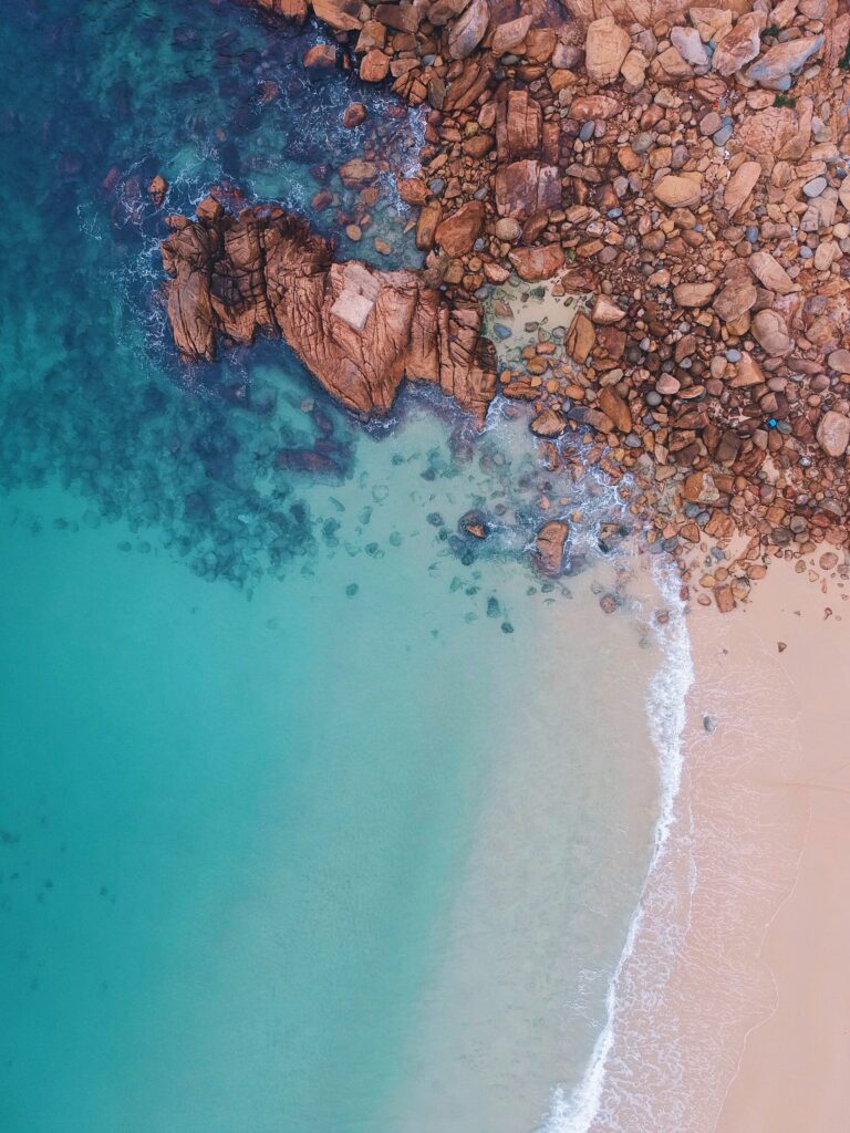 Aerial view of turquoise ocean meeting sandy shores with rugged brown stones coastline wallpaper