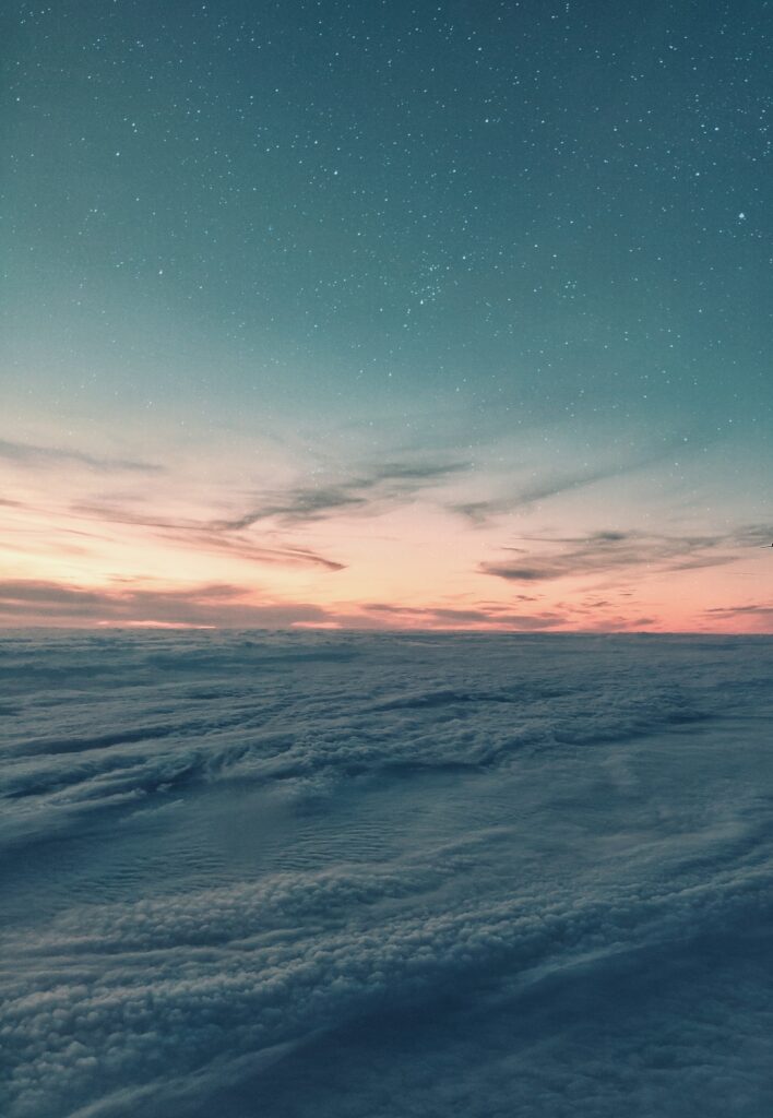 Aerial view of clouds at sunset blending warm pinks and cool blues into a starry night sky Wallpaper
