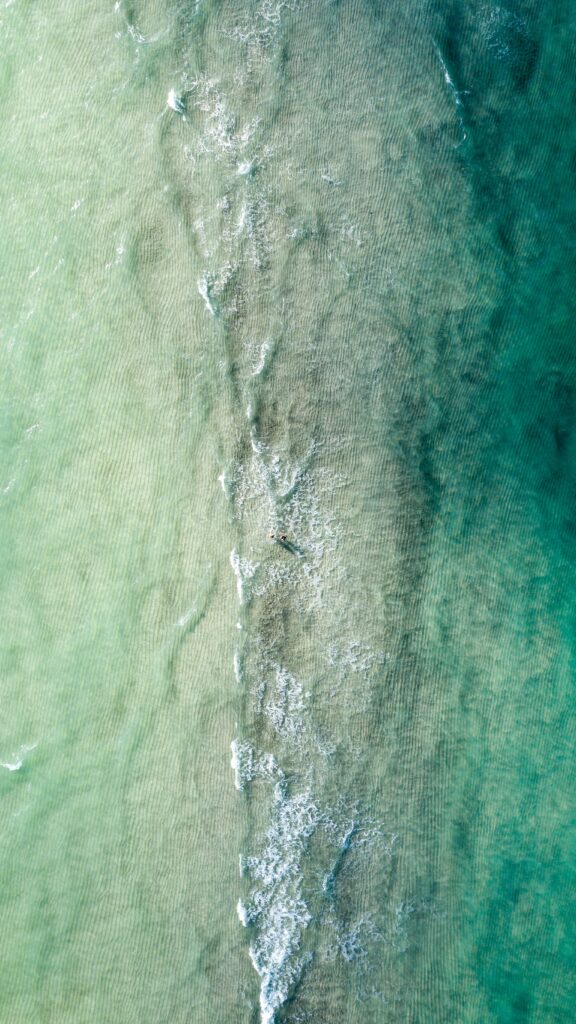 Aerial view of turquoise sea with gentle waves and soft ripples creating a tranquil ocean background Wallpaper