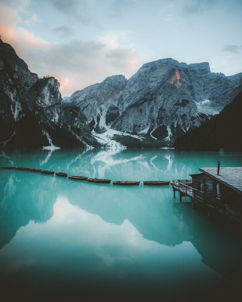 Tranquil bungalow by turquoise lake with snowy mountains reflecting in calm alpine water background Wallpaper