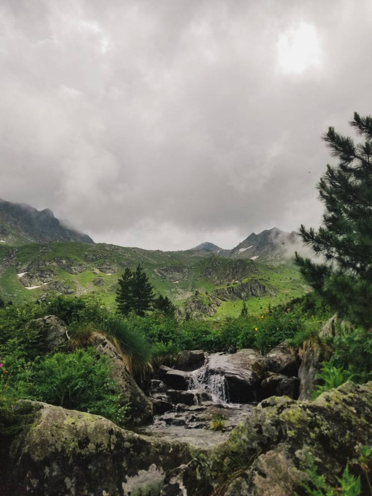Tranquil rocky stream flowing through lush green alpine mountains under moody cloudy sky wallpaper