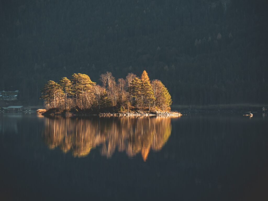 Tranquil island with autumn trees reflected in calm lake surrounded by misty forest wallpaper