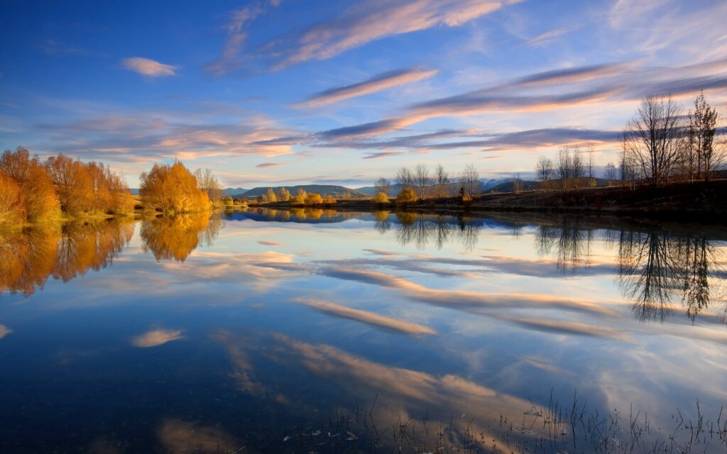 Tranquil autumn lake with golden trees and soft clouds reflected on calm water wallpaper background