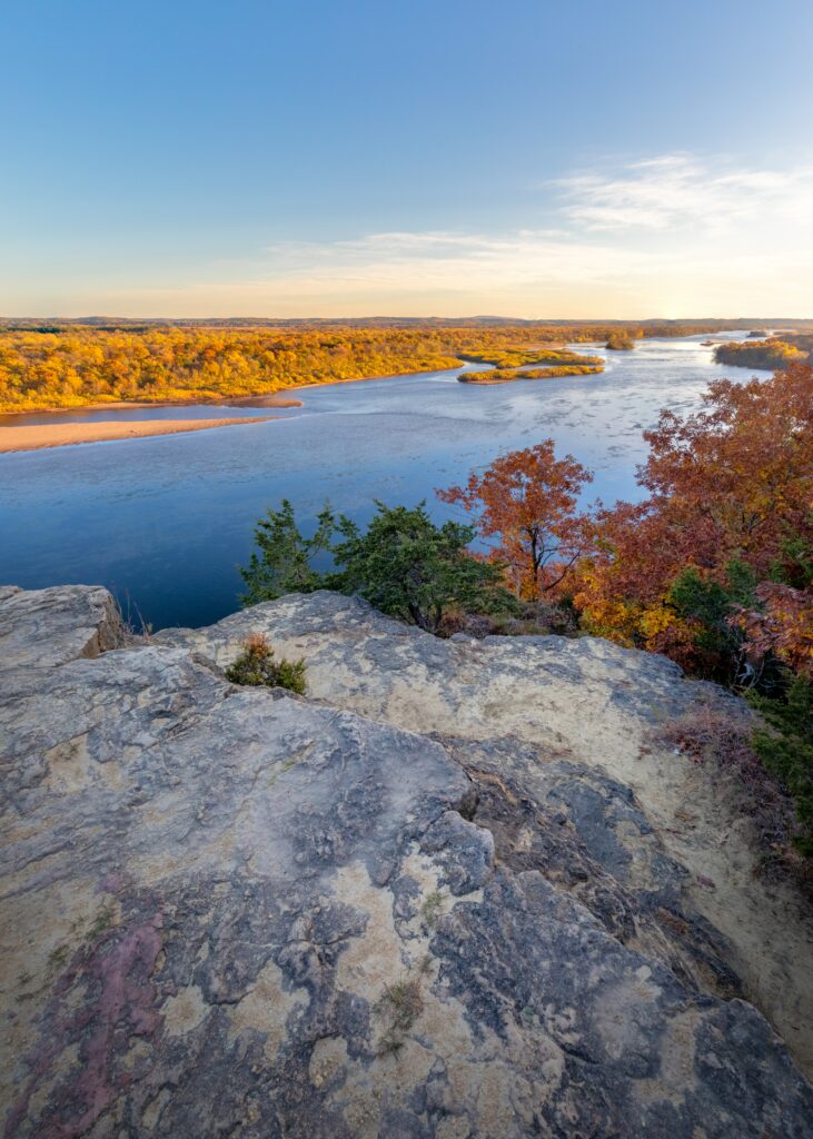 Tranquil autumn lakeside with golden trees rugged rocks clear blue water and natural shoreline Wallpaper