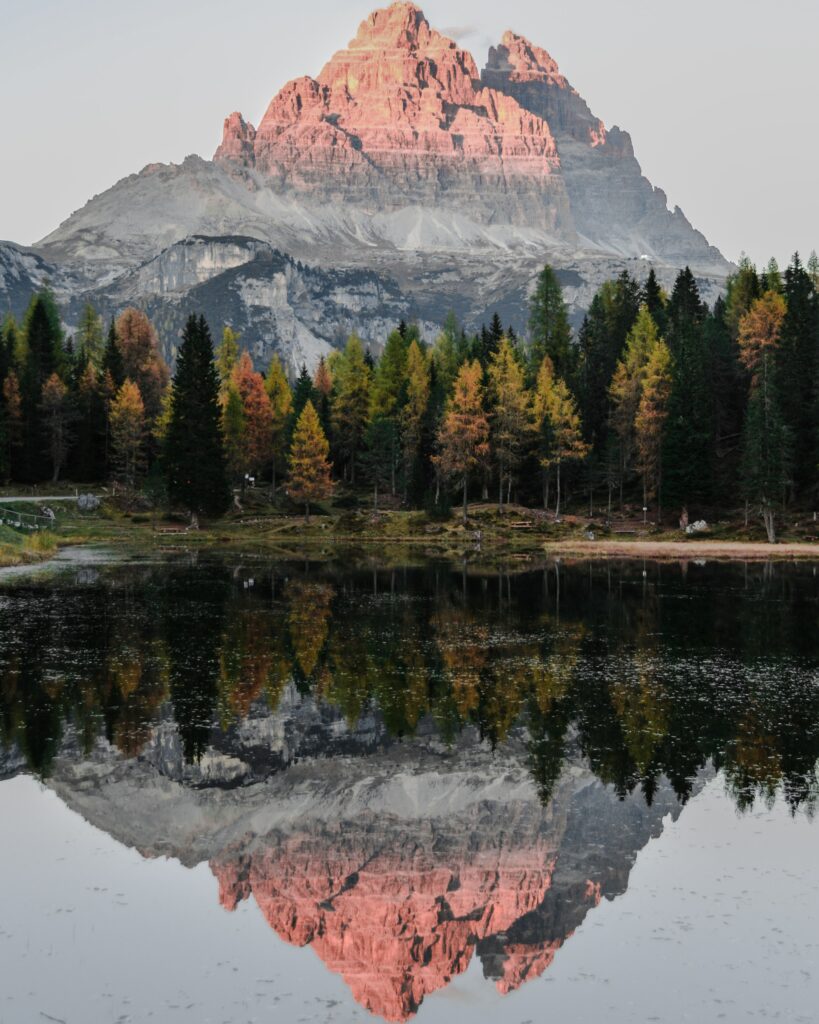 Mountain reflected in still lake with autumn trees and soft pink evening light wallpaper background