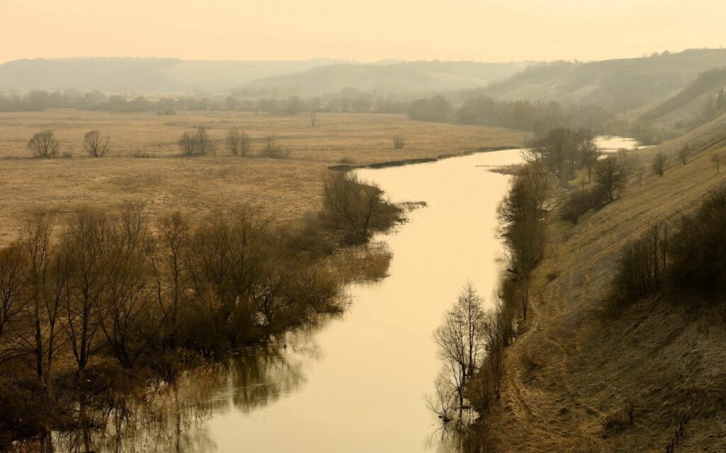 Peaceful river winding through golden fields and gentle hills in misty autumn Russia landscape Wallpaper