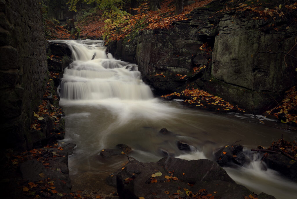Tranquil river flowing over smooth rocks mossy cliffs autumn leaves serene natural landscape wallpaper