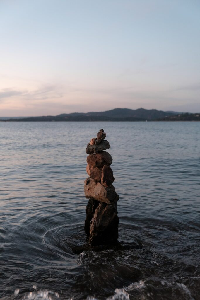 Balanced stone stack in calm sea waters at sunset with peaceful horizon and soft sky background Wallpaper